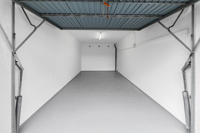Empty garage with white walls, gray floor, metal ceiling, and a single light fixture