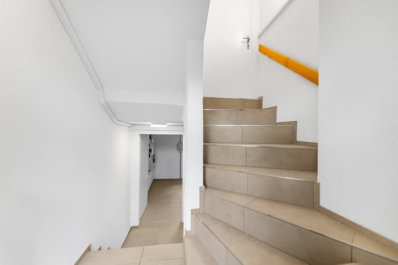 Modern staircase with beige tiles, white walls, and a yellow handrail