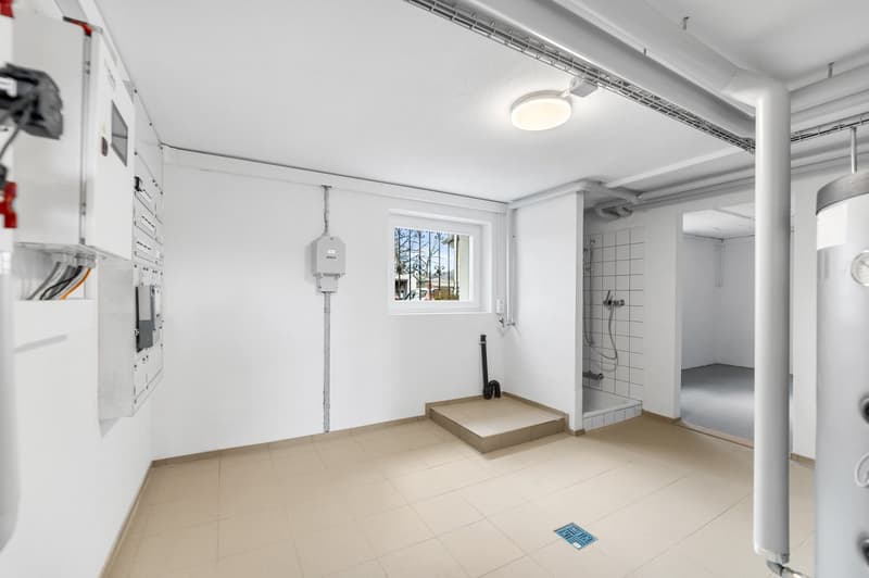 Empty room with tiled floor, white walls, electrical panels, small window, shower area, drain