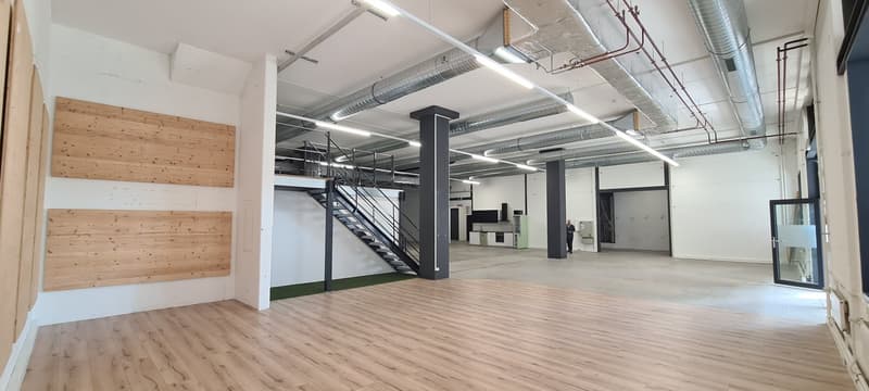 Large open commercial space with exposed ceiling, wooden wall panels, and a raised platform area. The space has a modern, industrial-style design with visible ductwork and lighting fixtures.