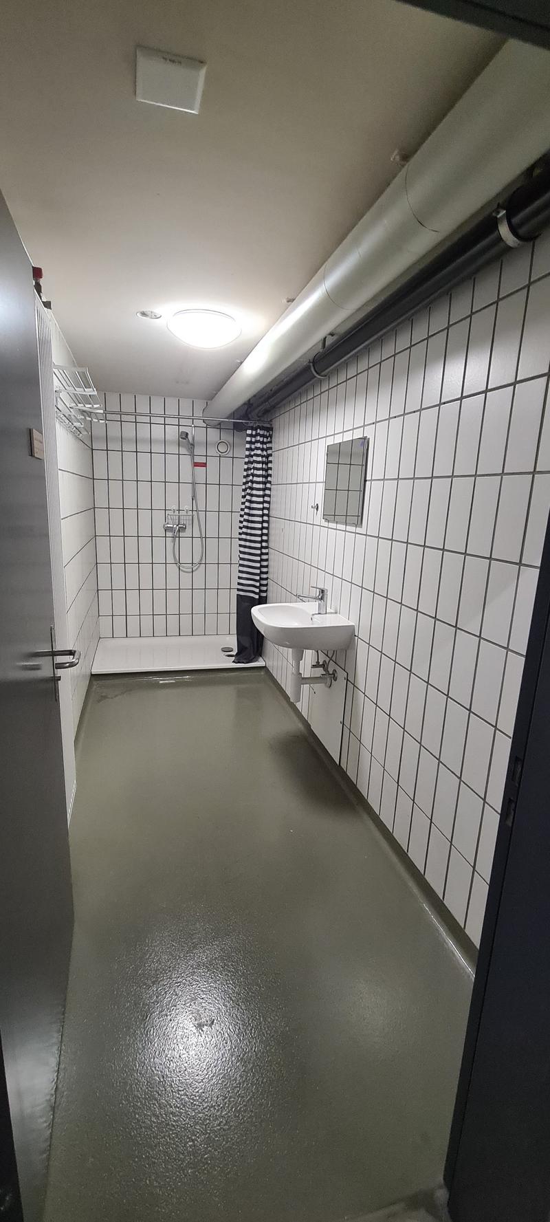 Tiled bathroom with a shower, sink, and a washing machine visible.