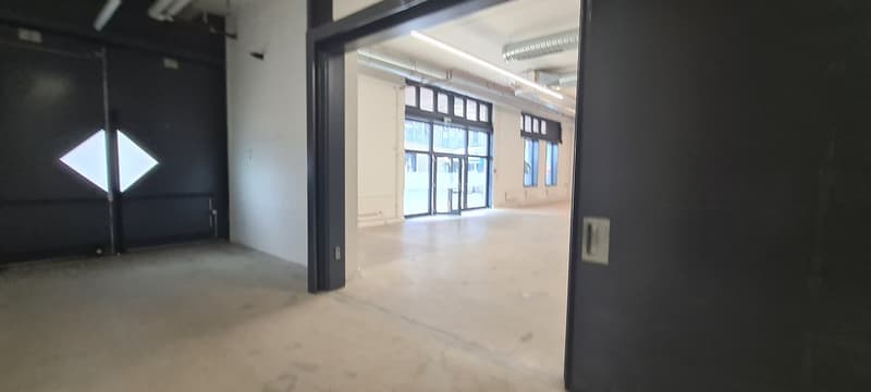 Large open commercial space with concrete floors, high ceilings, and large windows. The space appears to be unfinished or under renovation.