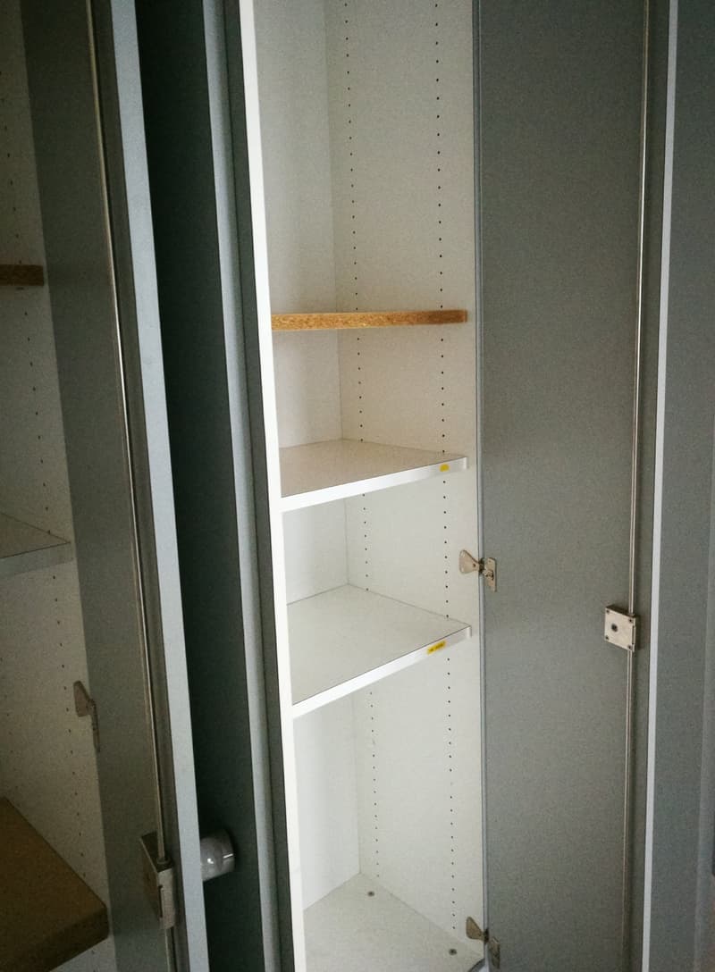 The image shows the interior of a closet with adjustable shelves. The closet has a white interior with a wooden shelf at the top. The closet has a door that appears to be made of glass or a transparent material.
