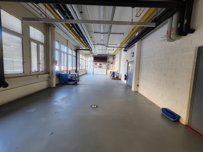 long hallway, white brick walls, gray floor, metal pipe beams, windows, fire extinguisher, trolley