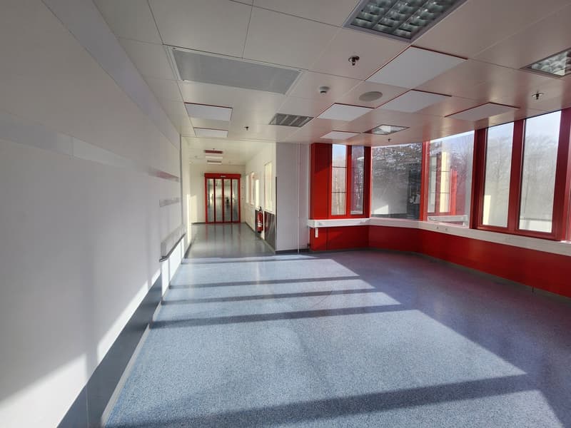 White and red walls, windows, tiled floor, empty hallway, surveillance cameras