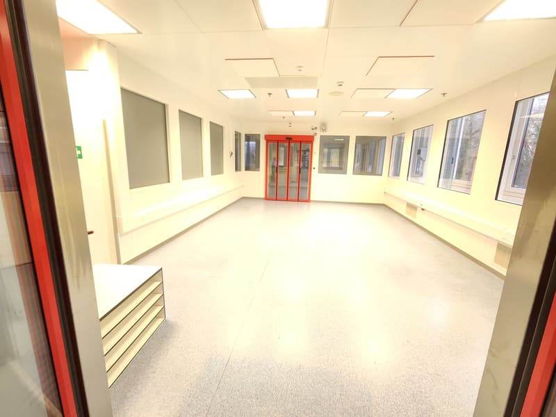 wide hallway, white ceiling, white walls, fluorescent lighting, windows, red door, white storage unit