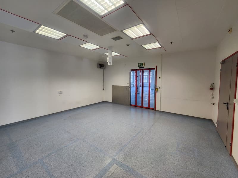 empty room, large space, gray floor, white walls, overhead lighting, two doors, air conditioning vent, glass door with red frames