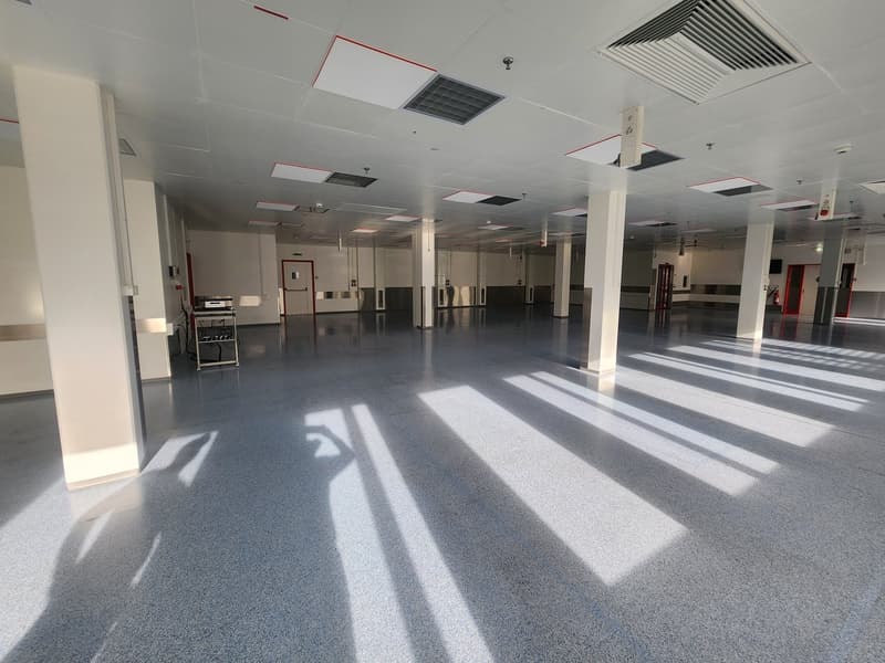 Open space, concrete floor, metal pillars, white walls, multiple doors, fire extinguisher