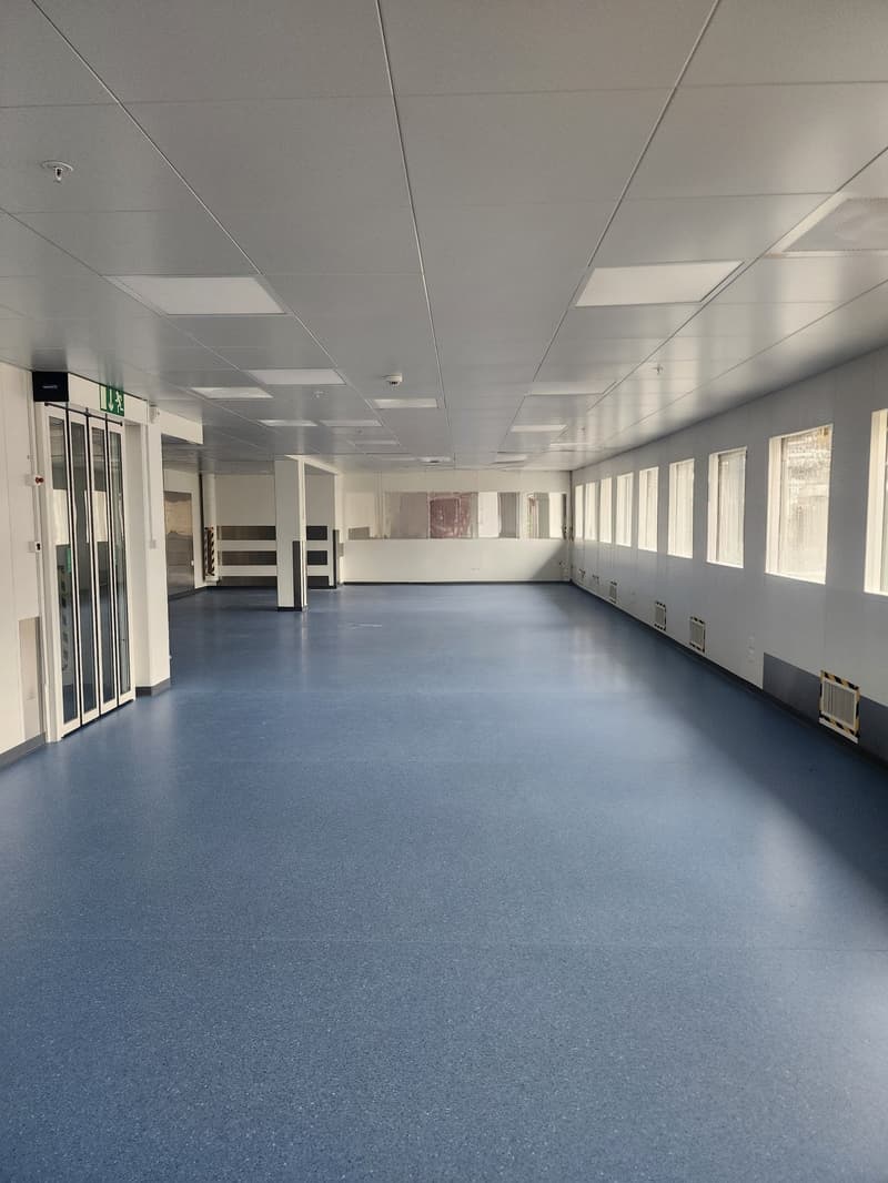 an empty room with blue flooring, white walls, large windows and square ceiling panels