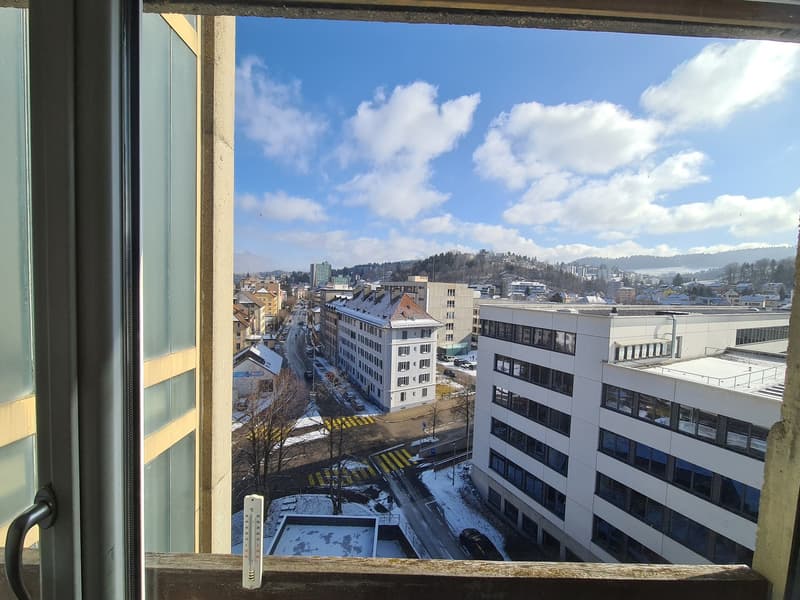 View from a window of a city with buildings, roads, and snow