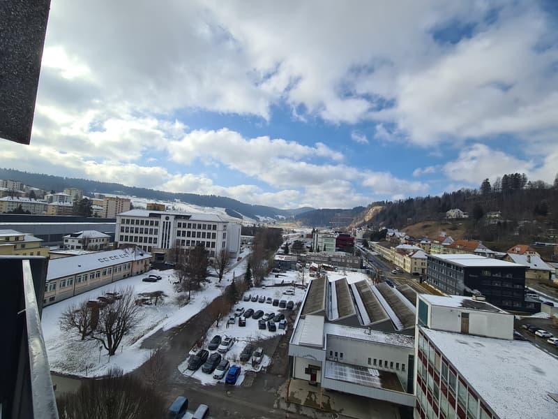 Aerial view of a city with multiple buildings, a parking lot, and a snowy landscape