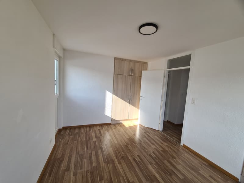 Empty room with wooden floor, white walls, wooden cabinet, open door, window, ceiling light