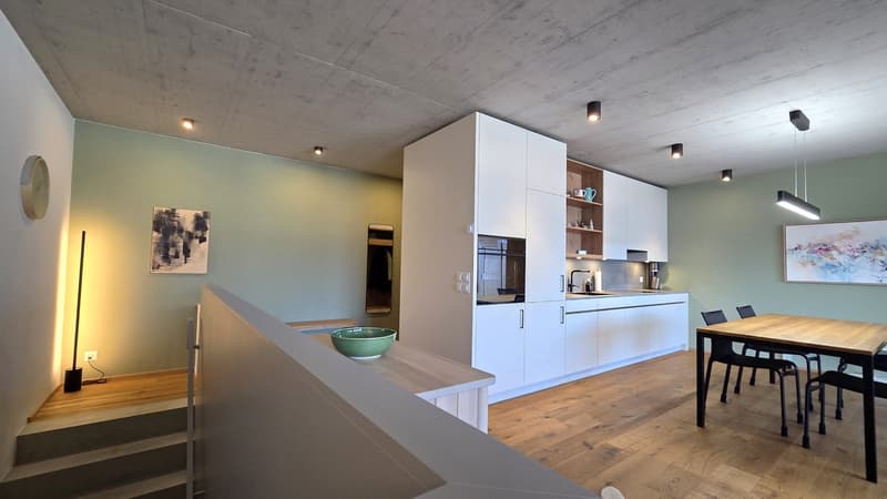 modern kitchen with wooden floor, white cabinets, wooden dining table, black chairs, green bowl, wall art, ceiling lights