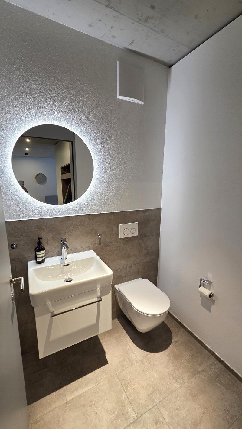 modern bathroom with white sink, white toilet, round mirror, tiled floor, white walls