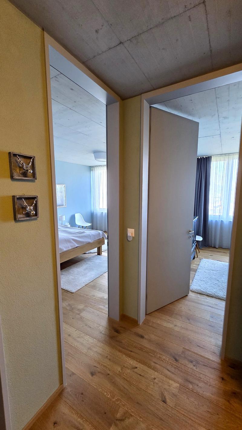 bedroom with bed, white rug, white walls, wooden floor, mirror, picture frames, white curtains, white chair, white lamp, white cabinet
