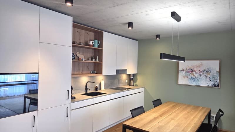modern kitchen with white cabinets, wooden dining table, black chairs, sink, faucet, countertop, shelves, picture frame, lamps
