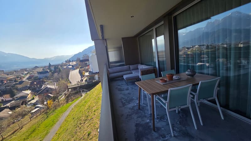 Balcony with table and chairs, couch, large windows, view of mountains and town