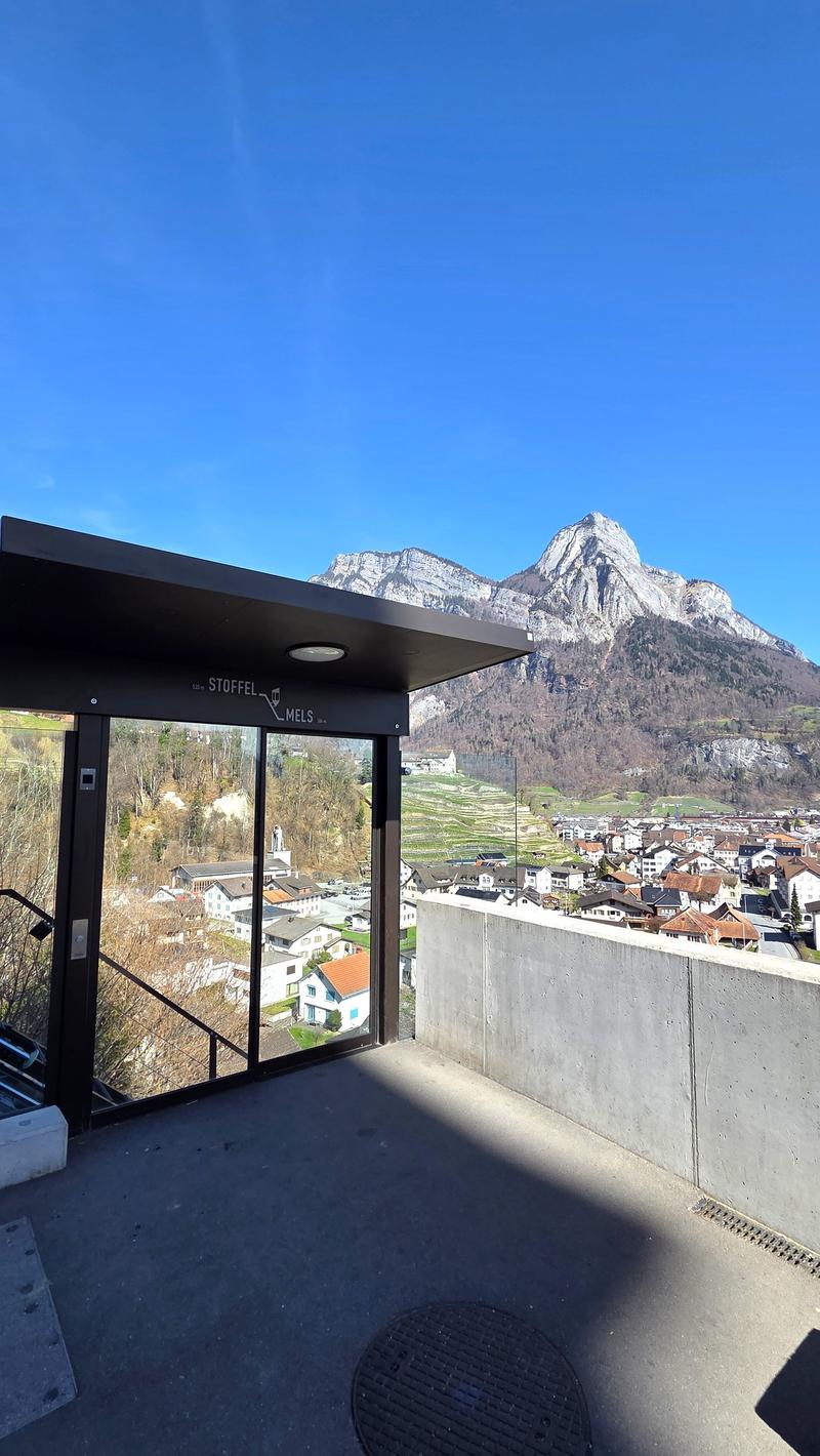 Balcony with glass doors, concrete wall, view of the mountains and village