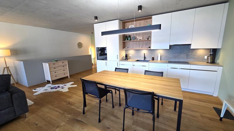 modern kitchen with dining area, wooden floor, white cabinets, wooden dining table, black chairs, white rug, lamp, dresser, open shelves, clock, microwave, sink, faucet, countertop