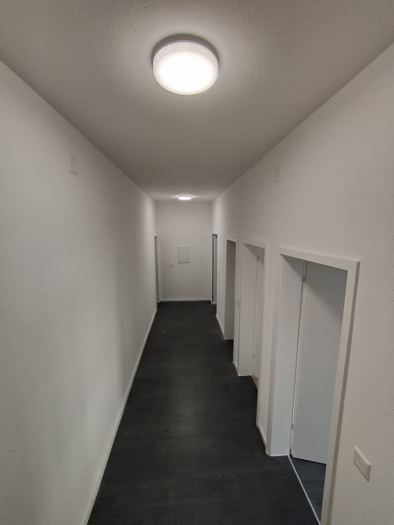 Empty hallway with white walls, black floor, ceiling lights