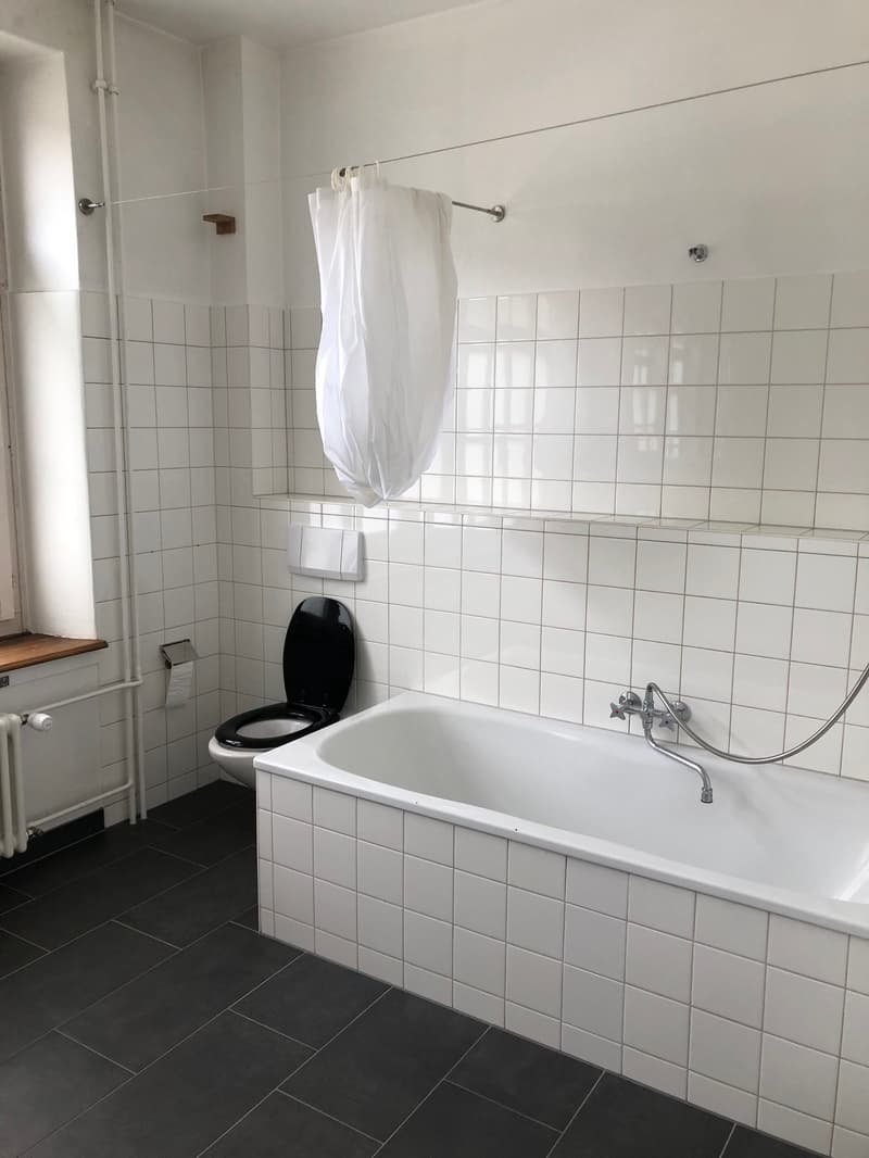 Bathroom with white tiles, black floor, white bathtub, black toilet, white shower curtain