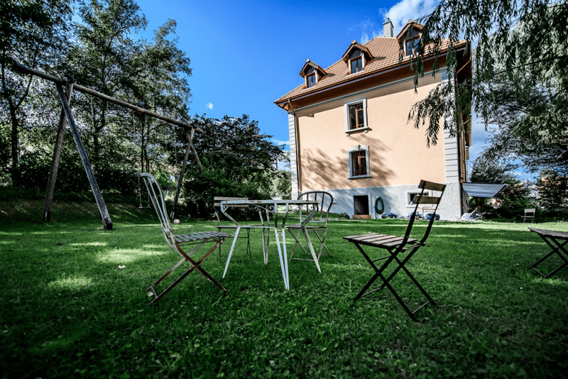 2 story house, beige exterior, red roof, garden, swing, table and chairs