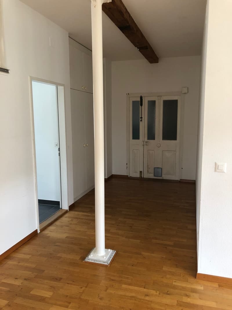 empty room, wooden floor, white walls, wooden beam on ceiling, central column, two doors, one leading to another room