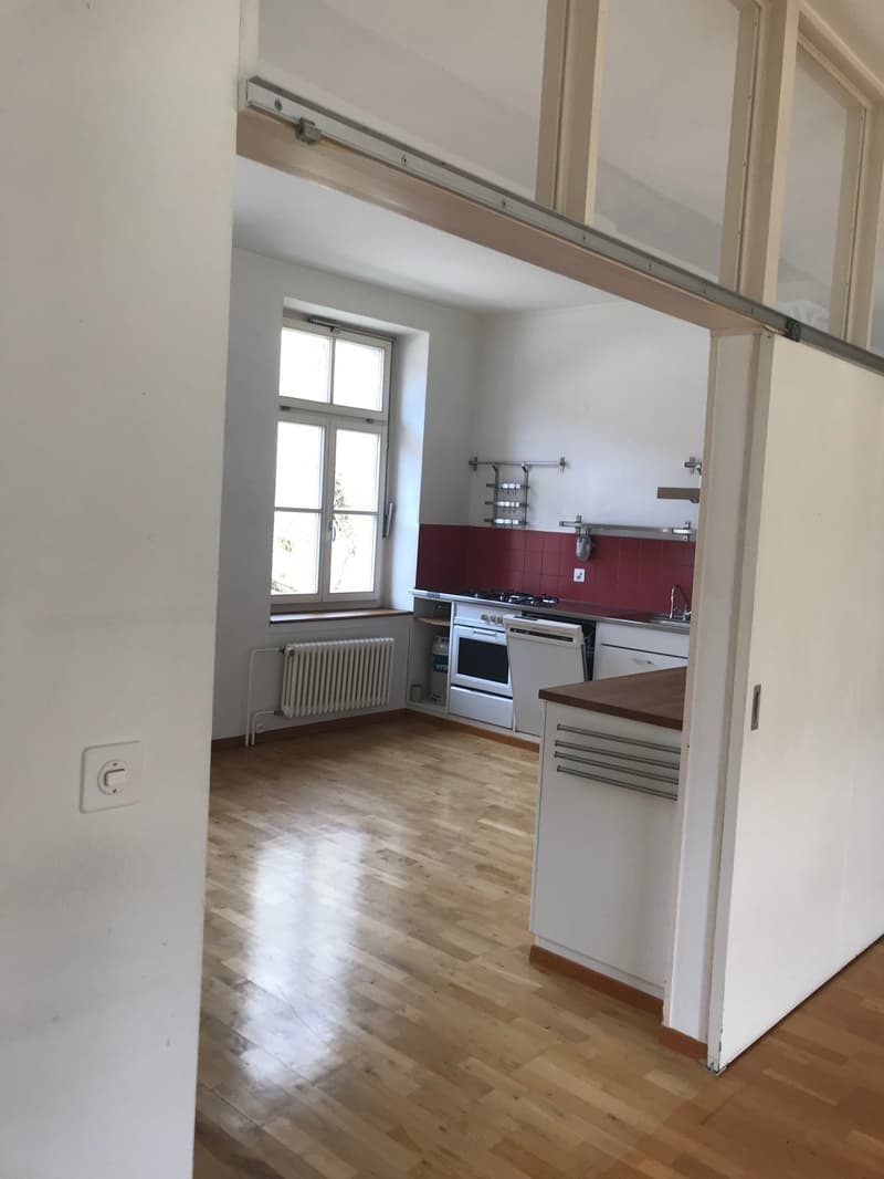 Empty kitchen with wooden floor, white walls, window, white appliances, red tiles on wall, radiator, wooden countertop, white cabinets, sink, faucet