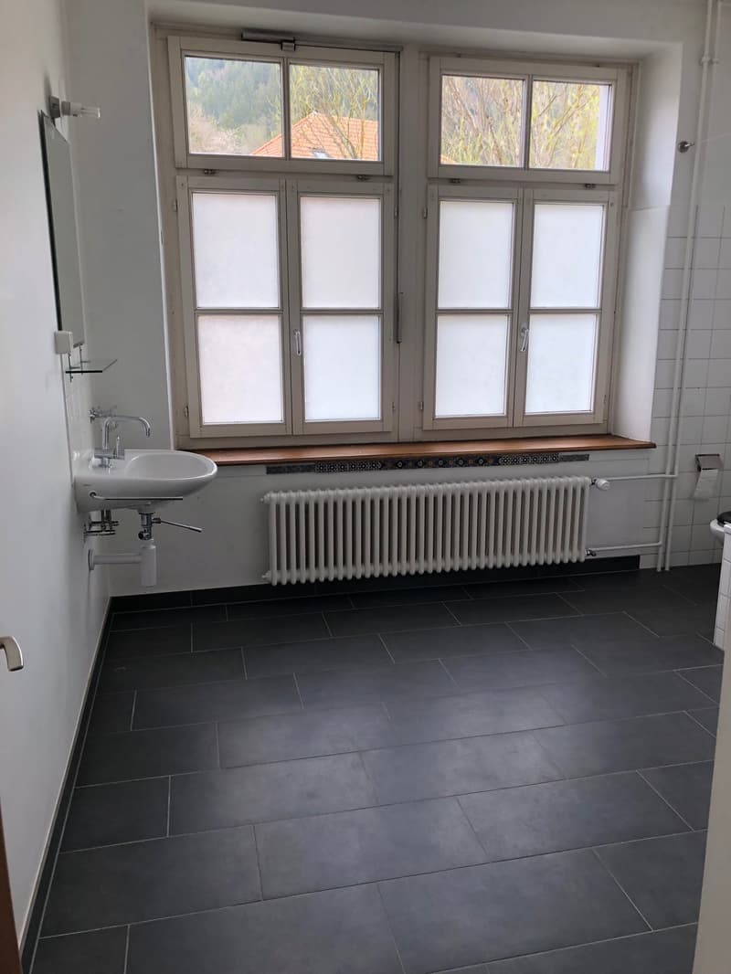 Bathroom with white sink, white radiator, black tiled floor, large windows, mirror