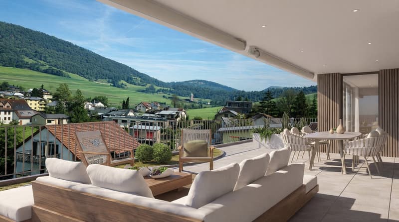 Furnished balcony with couch, chairs, table, cushions, pots, metal railing, view to village and mountains