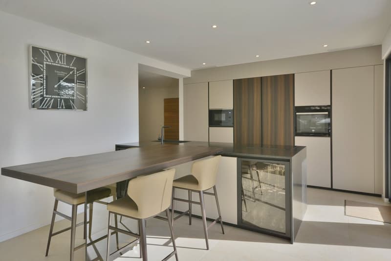 modern kitchen with island, wooden countertops, white cabinets, built-in microwave, sink, faucet, three bar stools, clock on wall