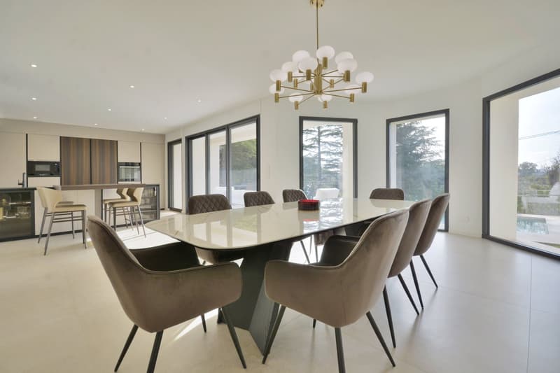 Dining room with large table, modern chairs, chandelier, glass doors, kitchen area, pool view
