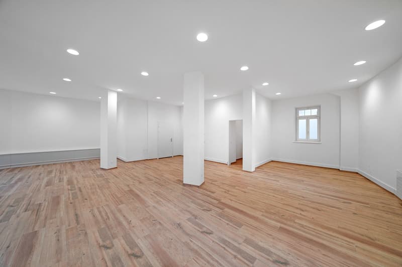 Empty room with wooden floors, white walls, and ceiling with recessed lighting.
