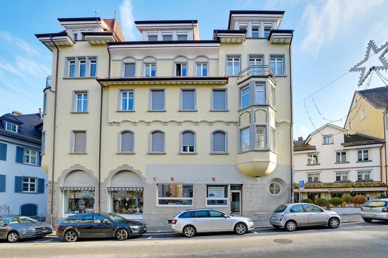 5 story building, beige facade, multiple windows, cafe on the ground floor, cars parked in front