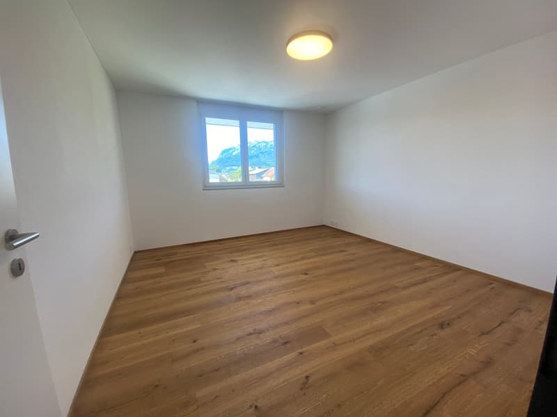 Spacious bedroom with hardwood flooring, white walls, and a large window providing natural light. The room appears to be empty, ready for furnishing and personalization.
