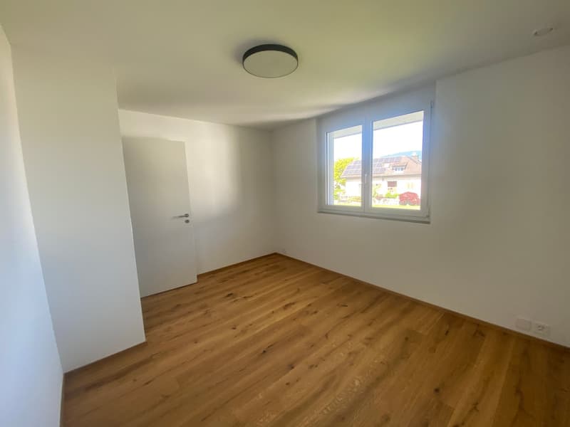 Spacious bedroom with hardwood flooring, white walls, and a large window providing natural light. The room appears to be empty, ready for furnishing and personalization.