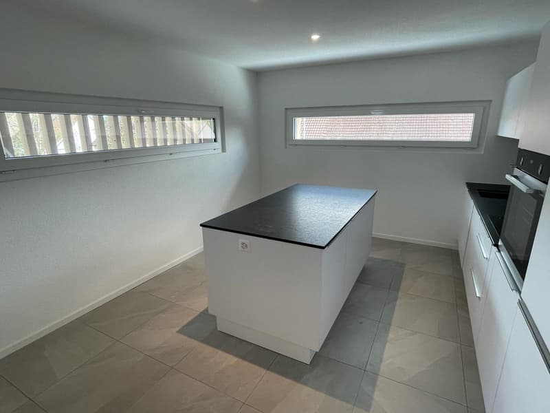 Open kitchen layout, white cabinets, grey tiles, central island with black countertop, appliances include oven and refrigerator.