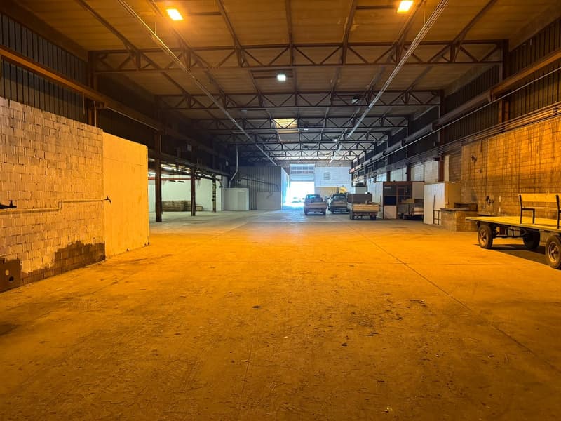 large industrial warehouse with brick walls, metal beams, concrete floor, several vehicles parked, large open space