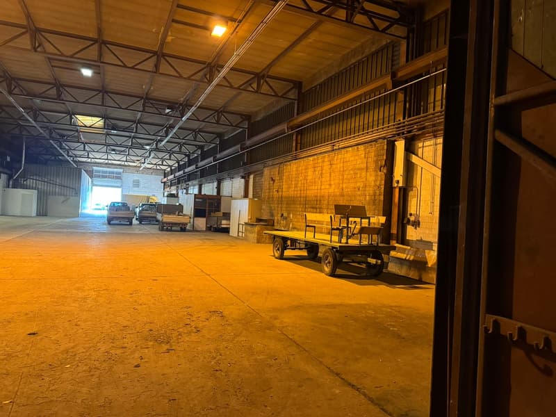 Open warehouse space, concrete floor, multiple cars parked, trackless trolleys, large doors, high ceiling beams