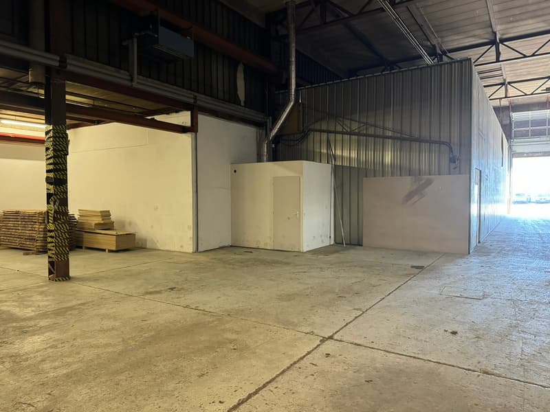 Large industrial warehouse, concrete floor, white walls, metal walls, large open space, stacked wood pallets, two white storage units.