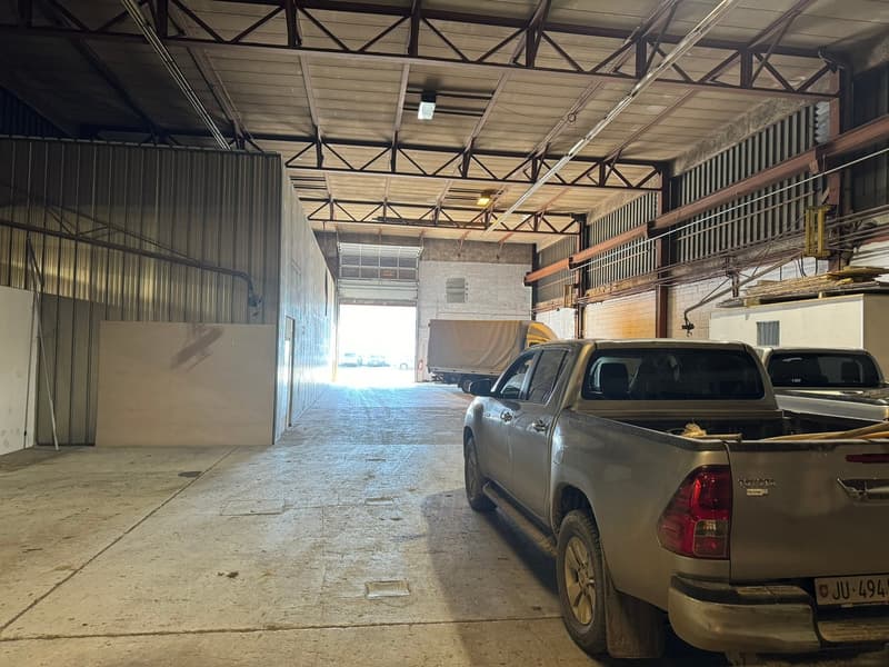 Industrial building with wide open space, large garage doors, pickup trucks parked, metal framework ceiling