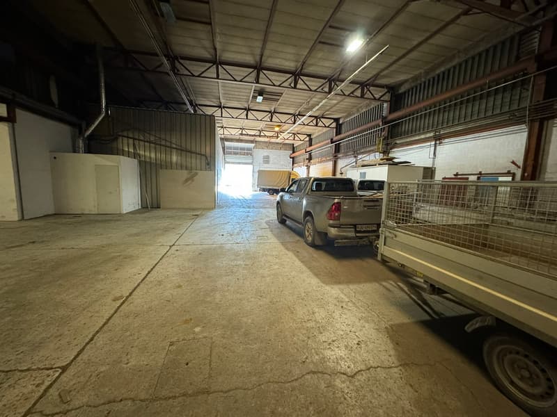 Warehouse with concrete floor, metal roof, two vehicles parked, storage boxes on the side, and a vehicle in the entrance.