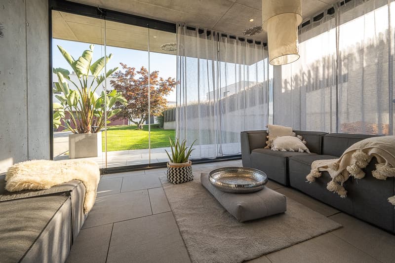 modern living room with large windows, glass doors, concrete walls, carpet, sofa, coffee table, plants, outdoor view
