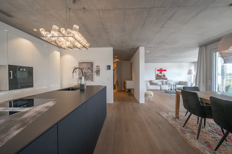 modern kitchen with black countertops, white cabinets, large chandelier, dining area with wooden table, white couch, rug, and artwork on the wall
