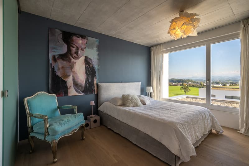 bedroom with bed, chair, lamps, painting, large windows, wooden floor