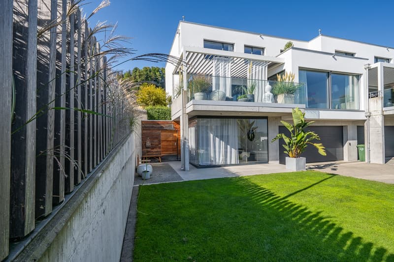 Modern white house, large glass windows, balcony with glass railing, two garages, well-maintained garden