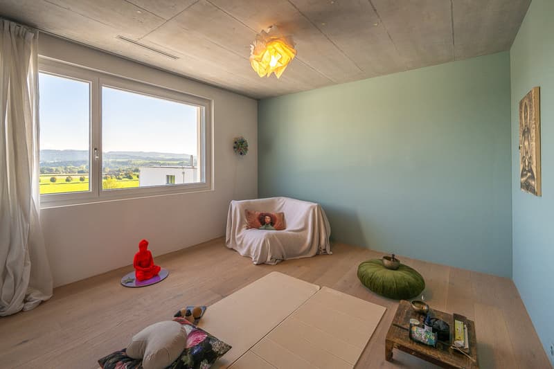 large window, wooden floor, white walls, covered chair, red statue, green cushion, table with bowls and objects