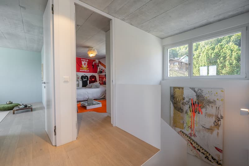 Open door leading to bedroom with bed, red banner, window with view of trees, artwork on wall