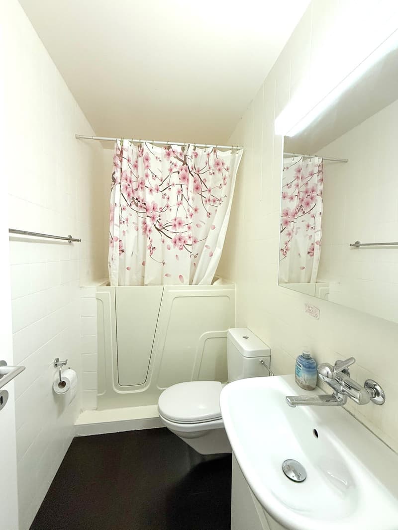 small white bathroom with white ceramic tiles, a toilet, a bathtub, and a sink with a mirror