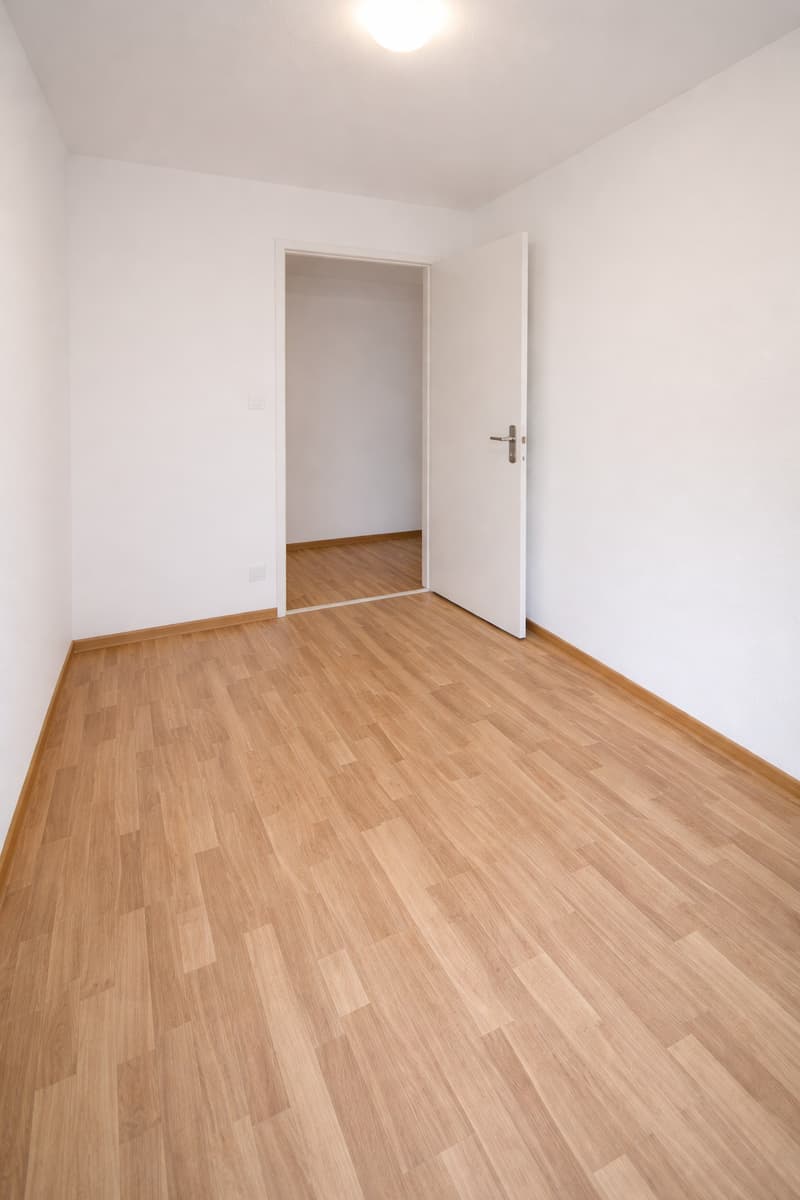 wood floor, white walls, bright ceiling light, open door to another room
